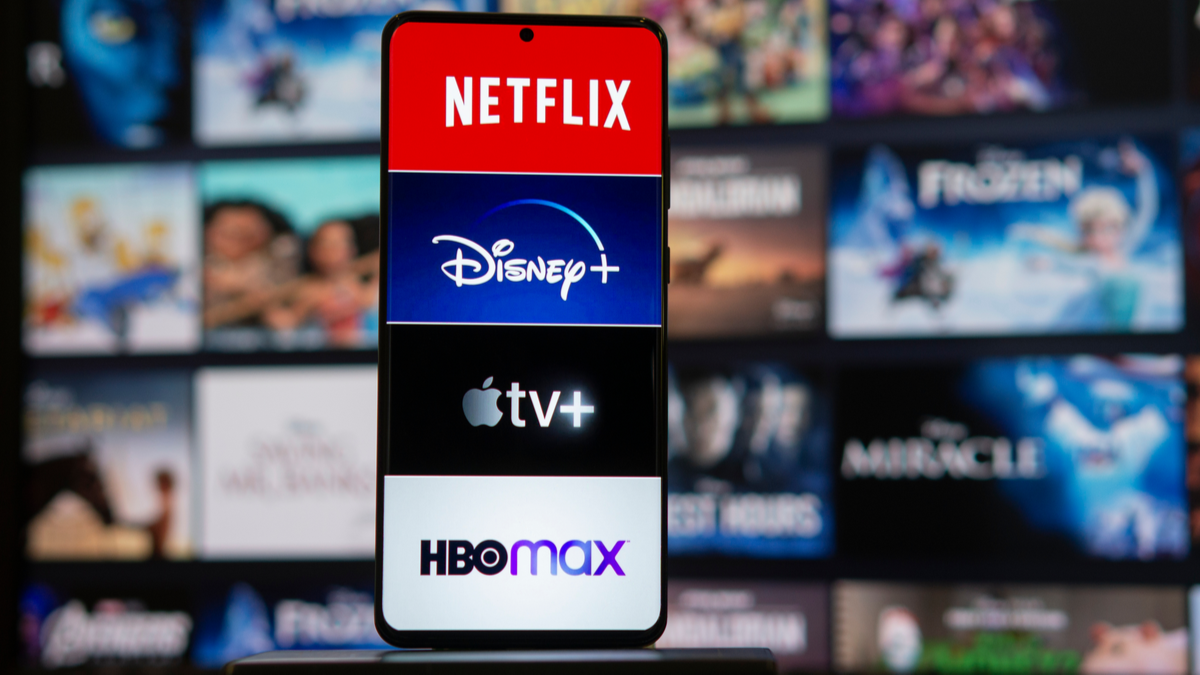 Netflix, Disney+, Apple TV+, and HBO Max logos on a phone in front of a TV.