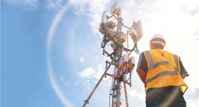 A worker standing beside a cell phone tower