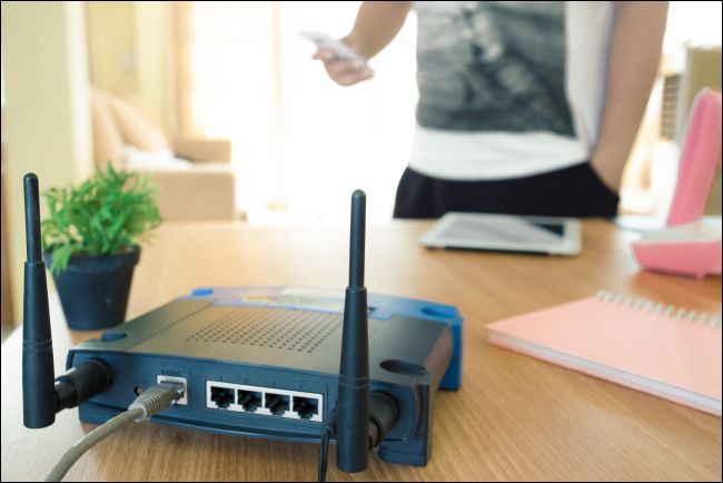 closeup of a wireless router and a young man using a smartphone on living room at home with a window in the background