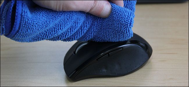 A hand wiping a computer mouse with a blue cloth.