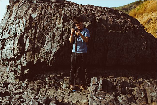Man adjusting camera on monopod in front of cliff face