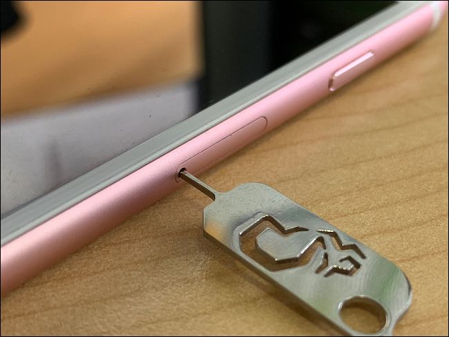 A SIM card removal tool inserted into the side of an Apple iPhone