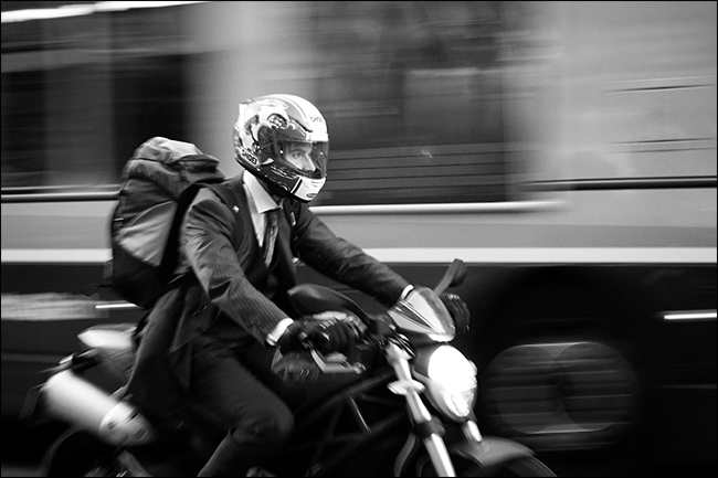 man in suit riding motorcycle with blurred bus moving behind him