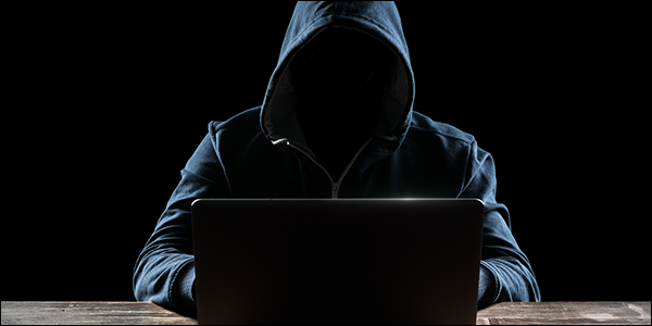 mysterious nerdy man in a hoodie hacking into a laptop
