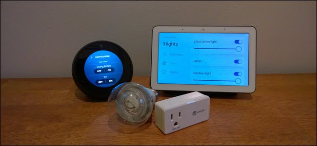 An Echo Spot, Google Home, Smart bulb and smart plug on a wooden surface.