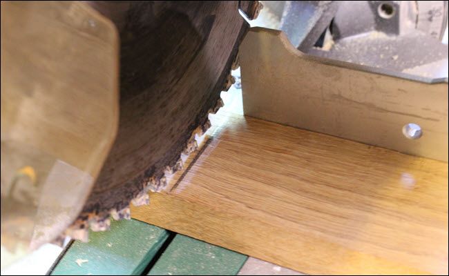 A board on a miter saw with a drawn line, the blade to the left of the line.