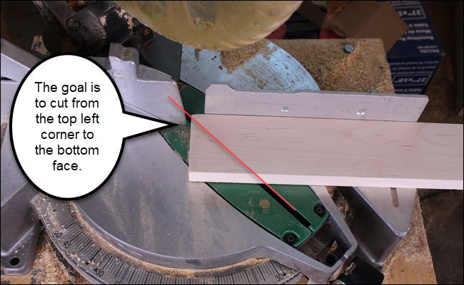 Board on a miter saw, with a 45-degree line drawn on it to show a short cut.