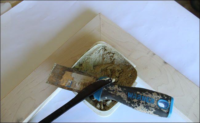 A corner of the frame with wood filler, a putty knife, and a plastic knife.