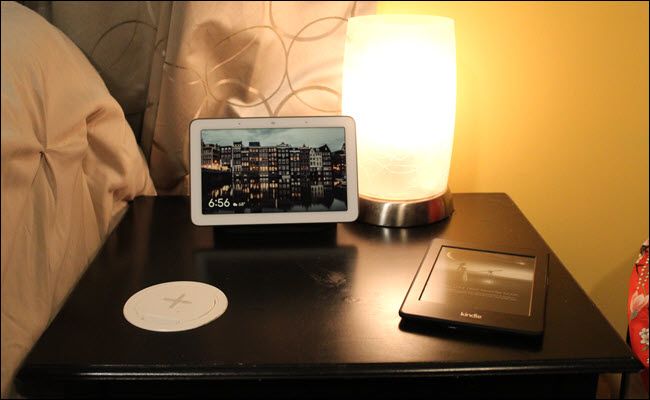 A nightstand with a wireless charger set into the surface, a kindle, and Google Home Hub