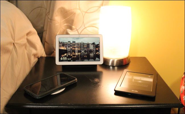 A Nest Hub, wireless charger, lamp with smart bulb, and kindle.