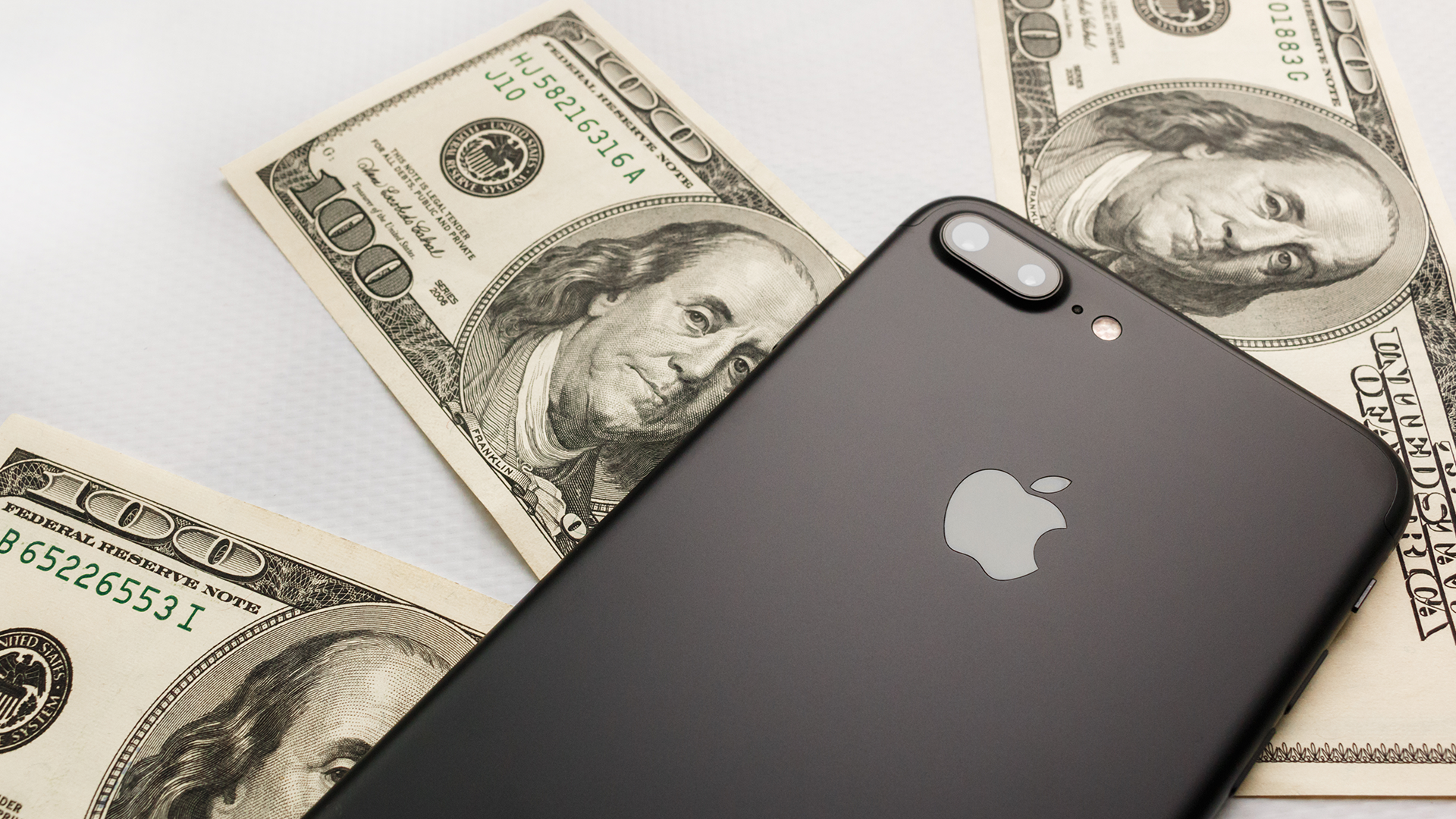 An iPhone X lying on top of three, $100 bills.