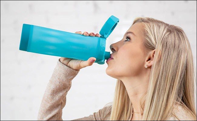 A woman drinking from a smart water bottle.