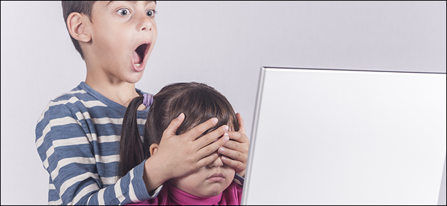 A little boy covers his sister's eyes at the computer.