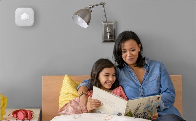 A mother and child reading a children's book in bed, with a Nest Protect mounted on the wall above their heads.