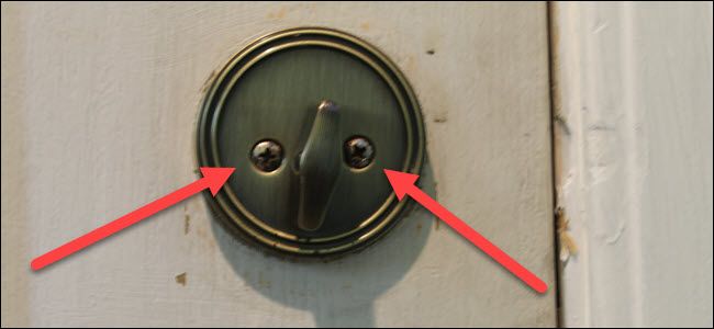 A standard thumbturn on a lock,with two red arrows pointing to two screws.