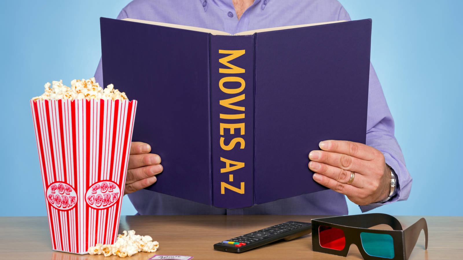 A person holding a book titled &quot;Movies A-Z&quot; and some popcorn