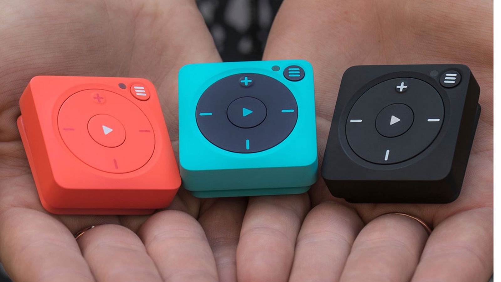 Someone's hands cupped and holding three Mighty Vibe players in red, blue, and black.