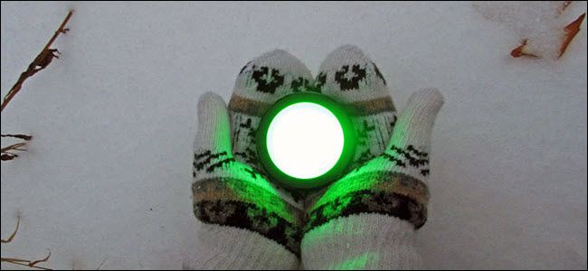 A pair of gloved hands holding an Echo button glowing green over the snow.