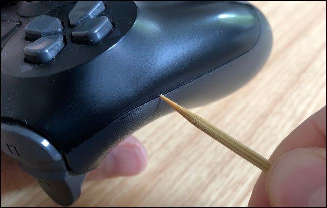 A hand cleaning a crevice on the side of a DualShock 4 with a toothpick.