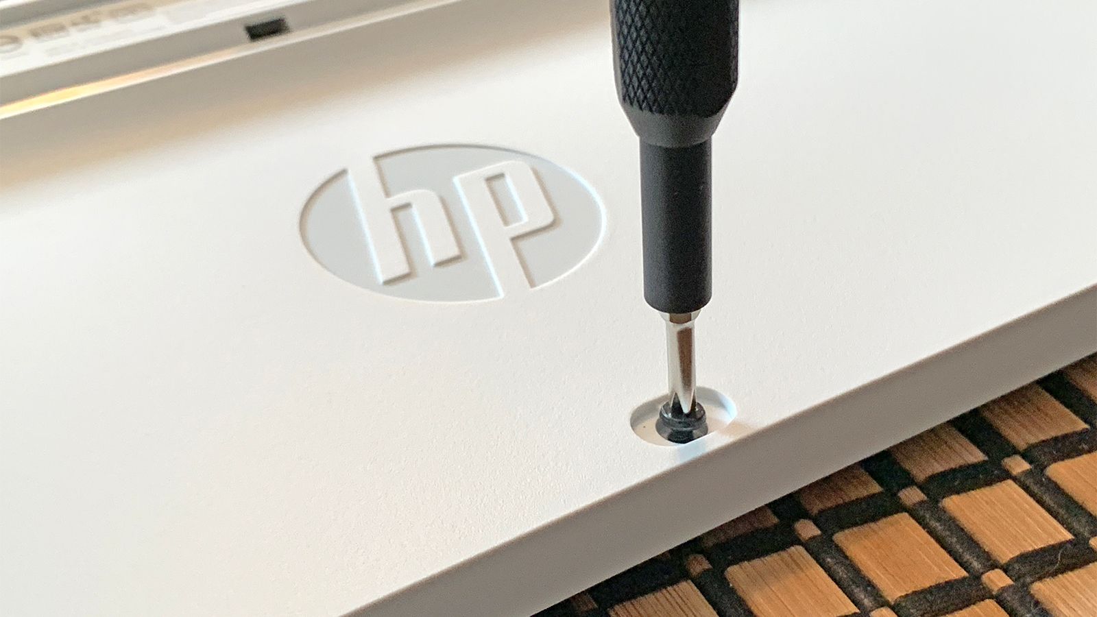 A screwdriver removing a screw on an HP keyboard.