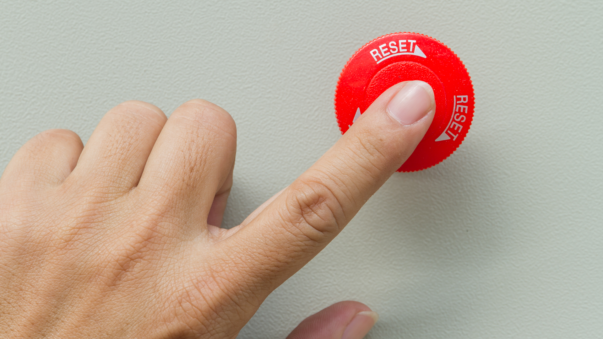 A finger presses a red reset button.