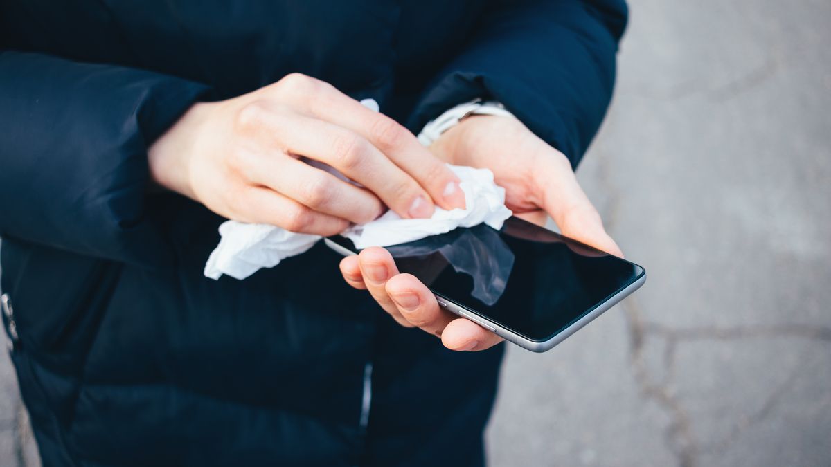 Hands holding and wiping a smartphone screen with a cloth.