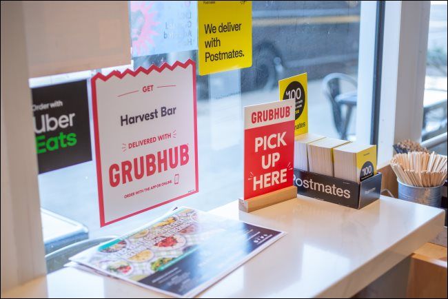 Signs for GrubHub, Postmates, and Uber Eats in a restaurant.