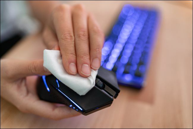 A hand wiping a computer mouse with a cloth.