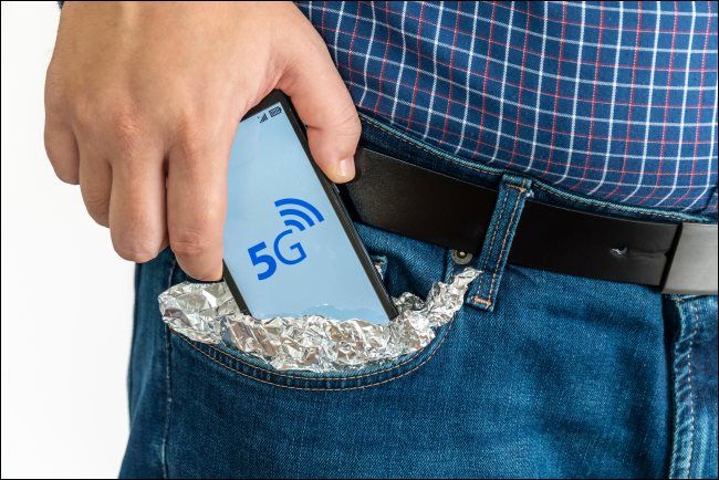 A man putting a 5G smartphone into his tin-foil-covered pocket.