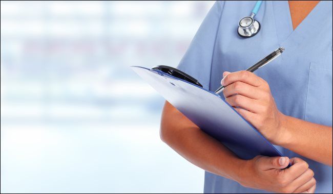 A person wearing scrubs writing on a clipboard.