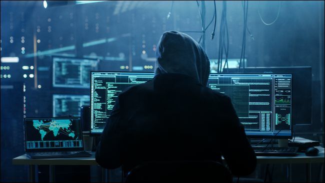 A shadowy hacker in a hoodie sitting in front of a computer.