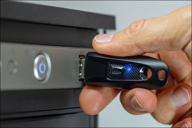 A hand inserting a USB flash drive into a desktop computer.