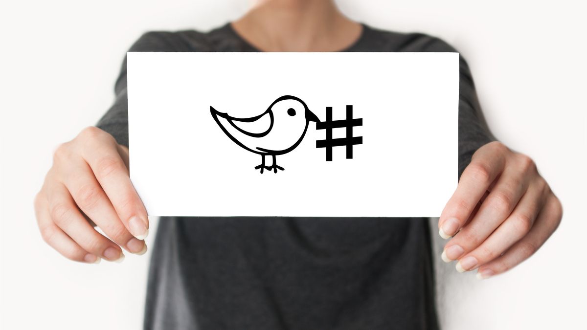 Someone holding a card with the Twitter bird drawn on it next to a hashtag