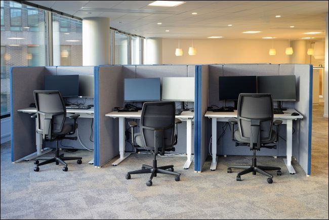 Three cubicles with matching chairs and computer monitors on the desks.