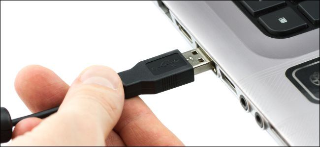 A hand plugging a USB Type-A cable into a laptop.