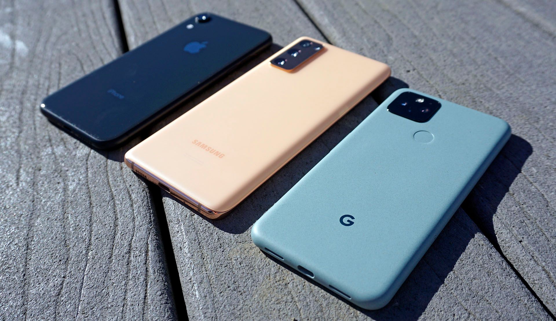 Comparing size: iPhone XR, Galaxy S20 FE, and Pixel 5, in a row on wood