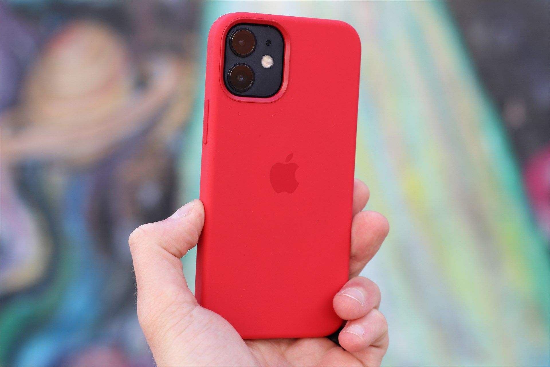 The black iPhone 12 Min in a red Apple case, colorful wall art in the background