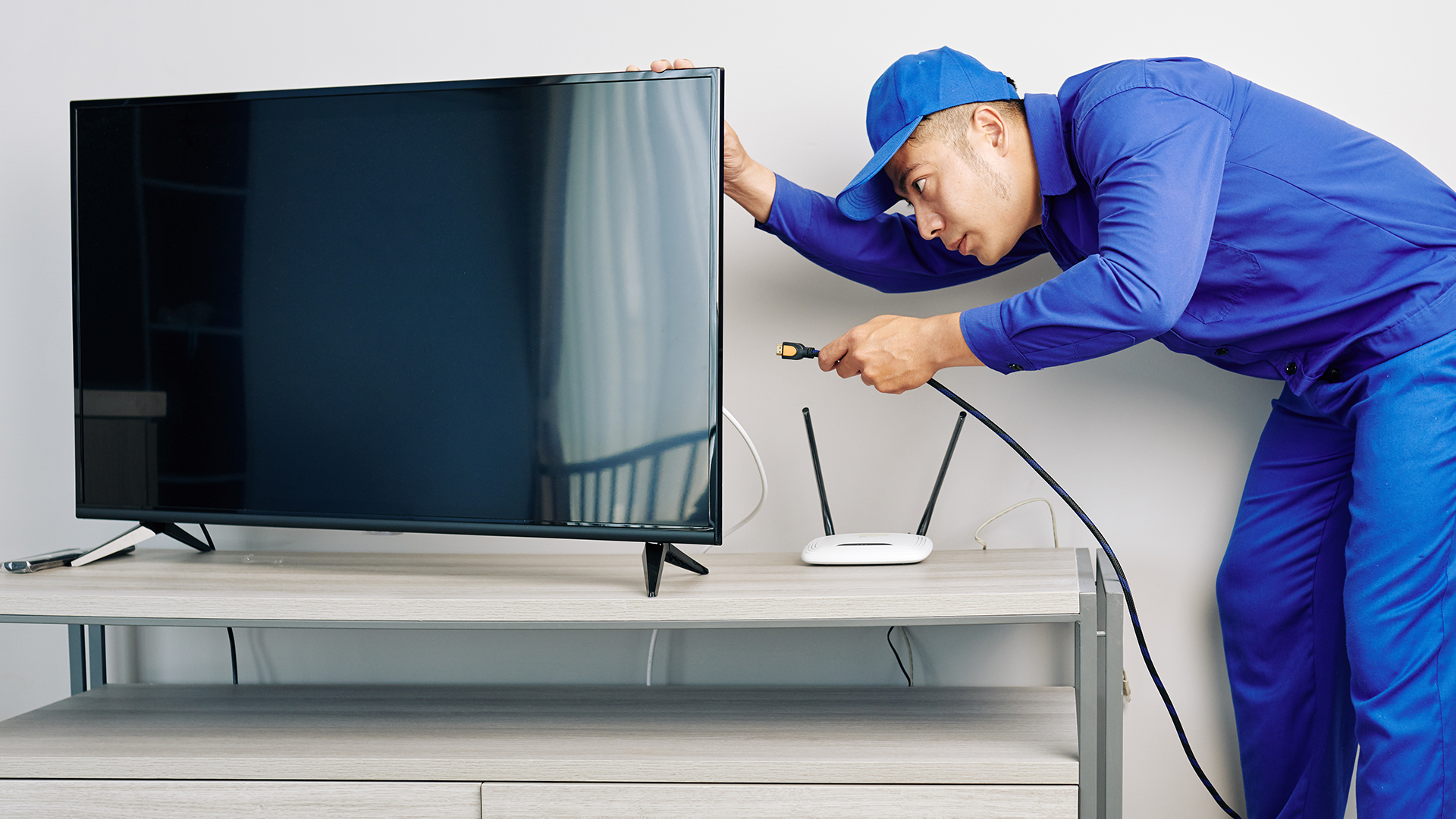 A cable technician plugging a coaxial cable into the back of a flatscreen TV.