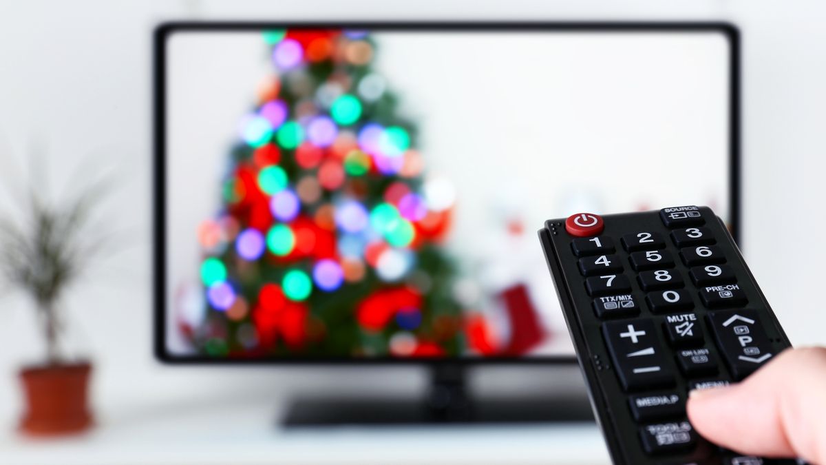 Person pointing a remote towards a TV playing a Christmas movie
