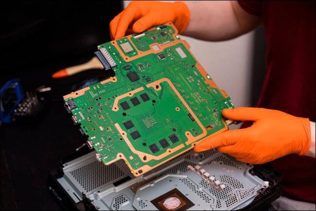 A person repairing the inside of a PlayStation 4 Pro console.