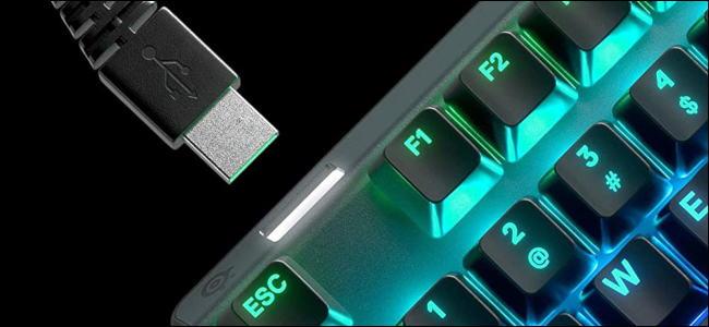 An RGB-illuminated keyboard with a USB cable being inserted into a USB passthrough port.