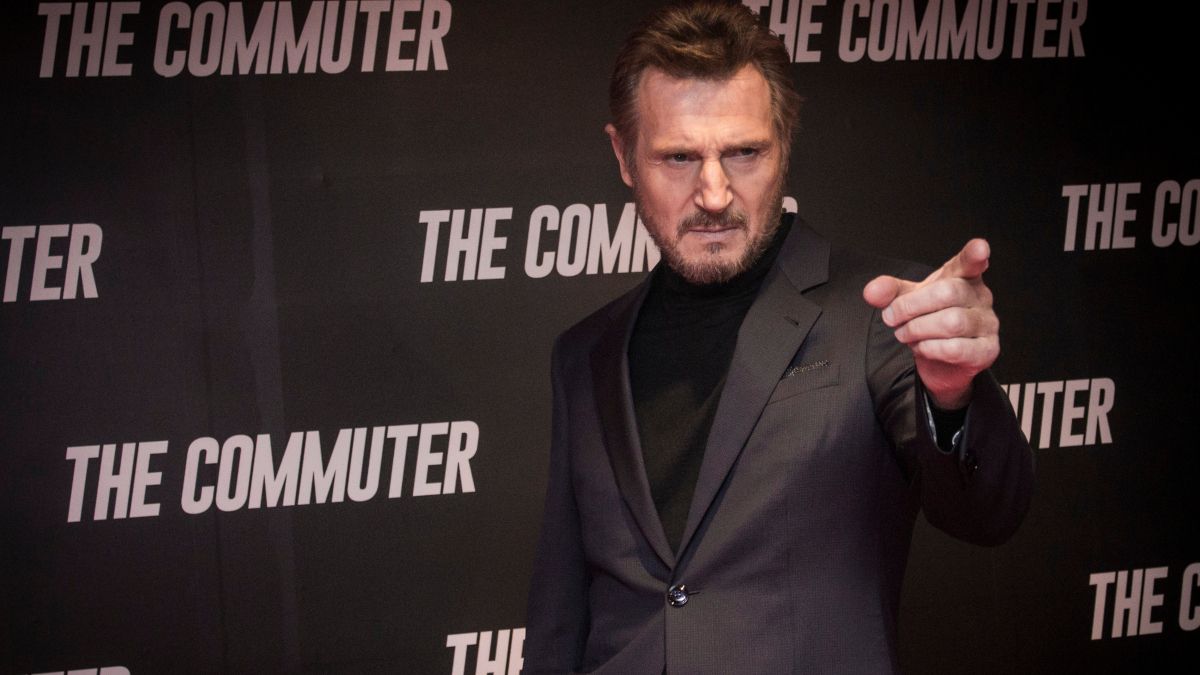 Actor Liam Neeson standing and pointing in front of a promotional banner for his movie 