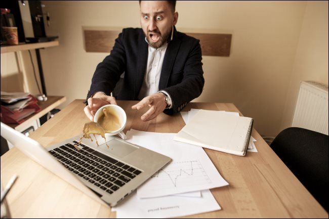 A man spilling coffee on a laptop.