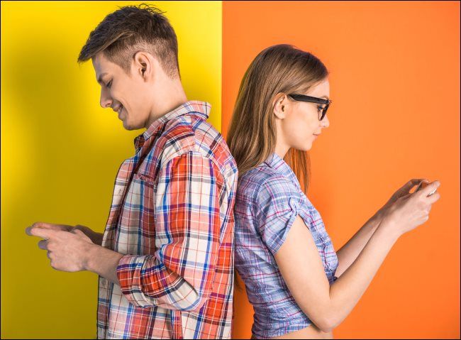 Young couple standing back to back and texting.
