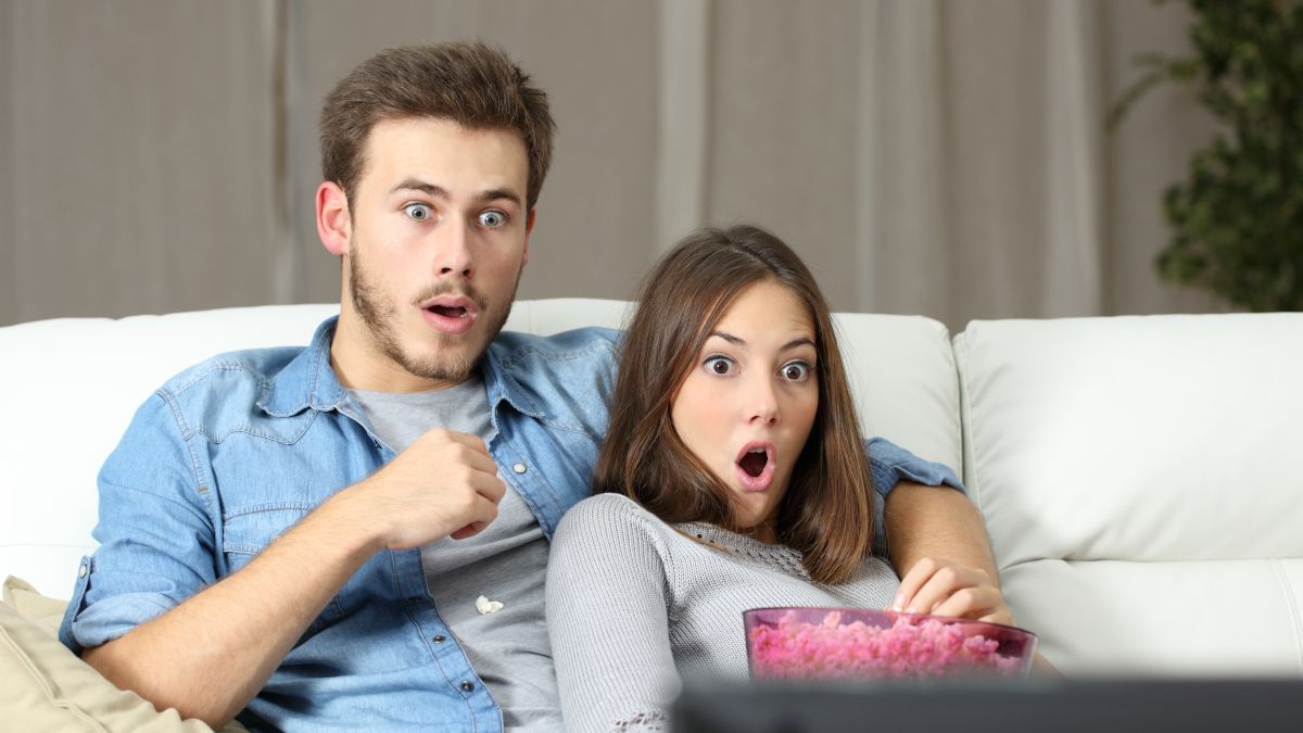 A young couple watching a TV with shocked or amazed expressions on their faces.