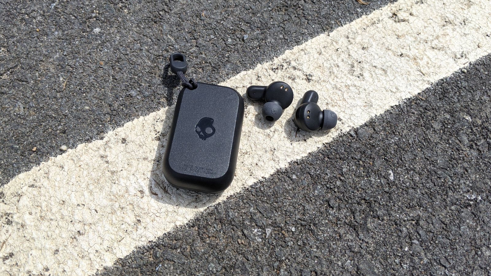 Skullcandy Dime case and earbuds separated on pavement