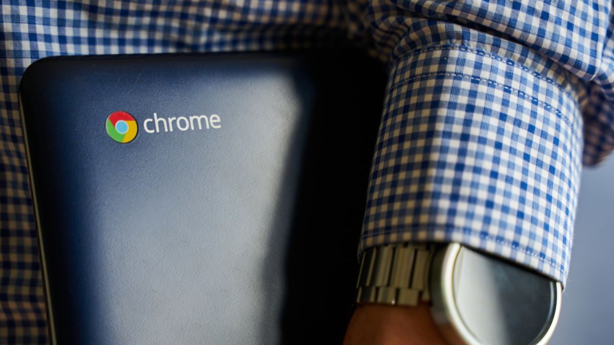 A person holding an Asus Chromebook under their arm.