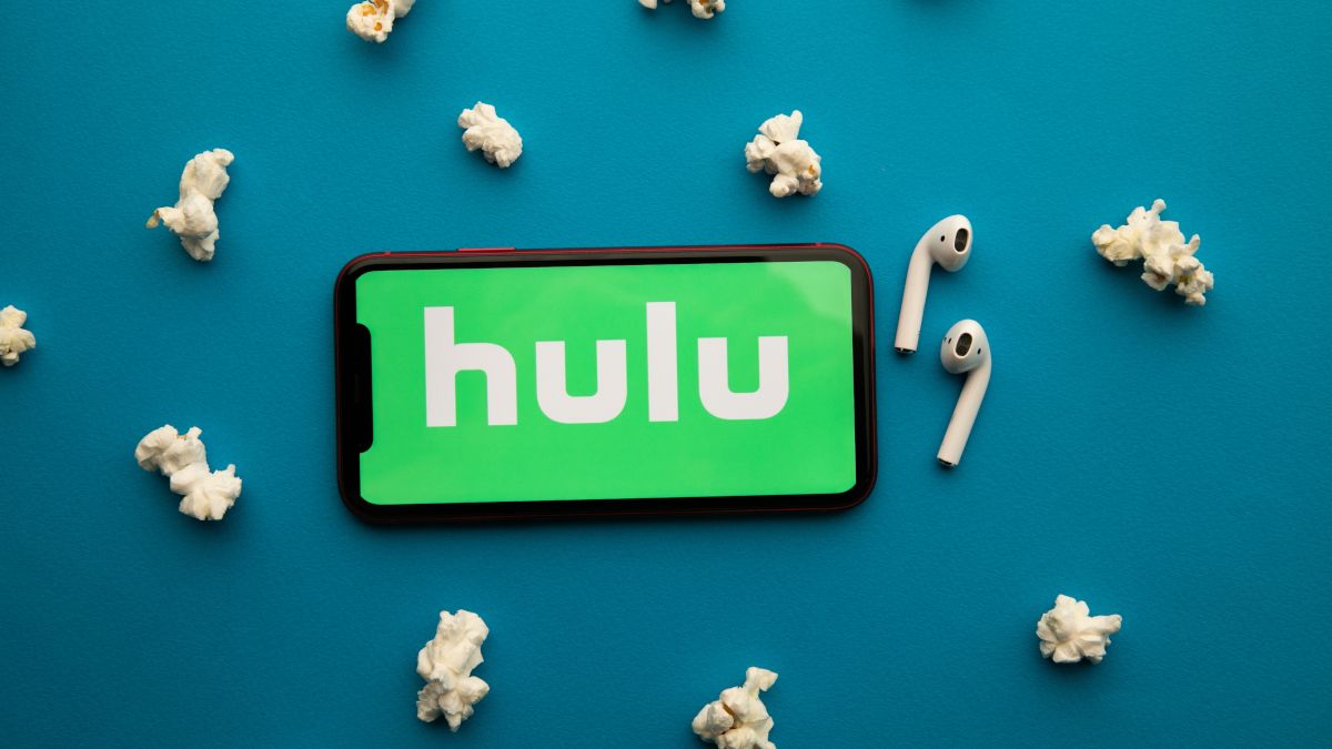 Hulu logo on an iPhone screen with wireless earbuds and popcorn surrounding it.