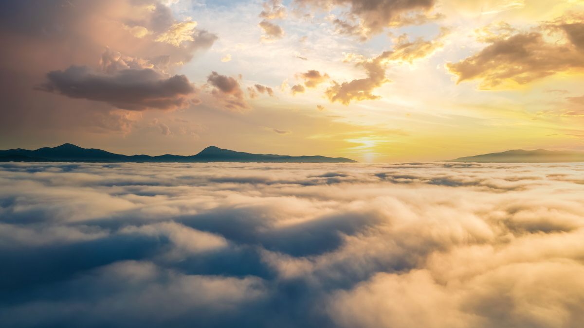 An aerial view of a sunset over dense clouds with mountains on the horizon.