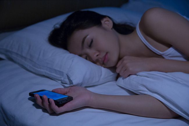 A woman sleeping while holding a smartphone.